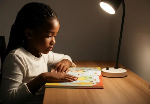 Jeune fille lisant un livre avec lampe de bureau éclairée