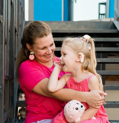 Avec un sourire, une maman et sa jeune fille portant un appareil auditif sont assises sur les marches de l'escalier