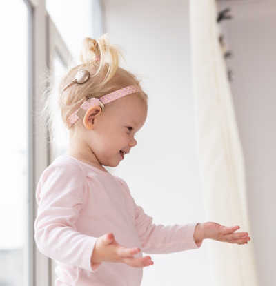 Petite fille vue de côté avec un implant cochléaire et qui allonge une main