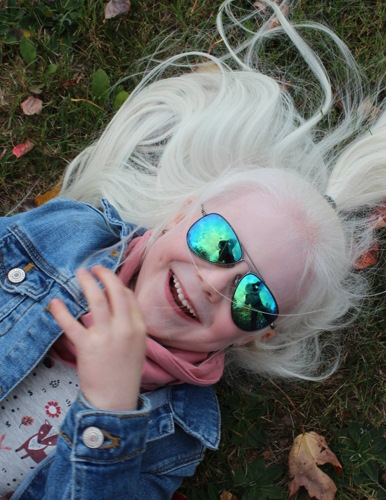 Jeune fille souriante aux cheveux blancs et portant des lunettes à soleil et couché dans le gazon