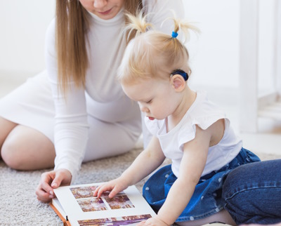 Une femme et une fillette portant un appareil auditif sont assises au sol pour regarder un album photo