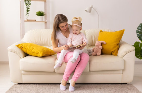Une femme et une fillette portant un implant cochléaire sont assises sur le sofa et regardent un livre