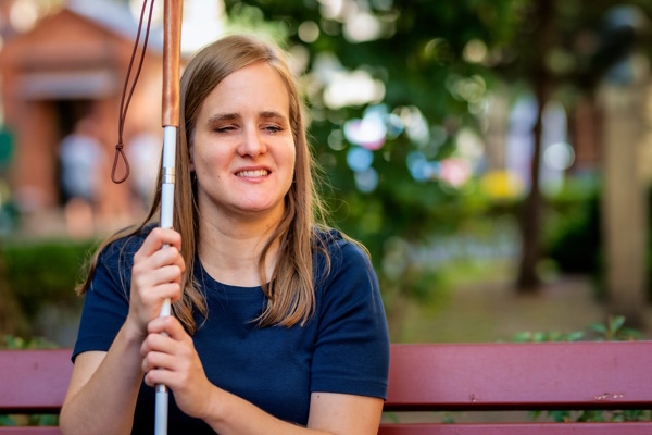 Jeune femme assise sur un banc de parc avec sa canne blanche à côté