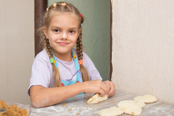 Jeune fille souriante avec farine sur le nez et travaillant la pâte à biscuit dans la cuisine