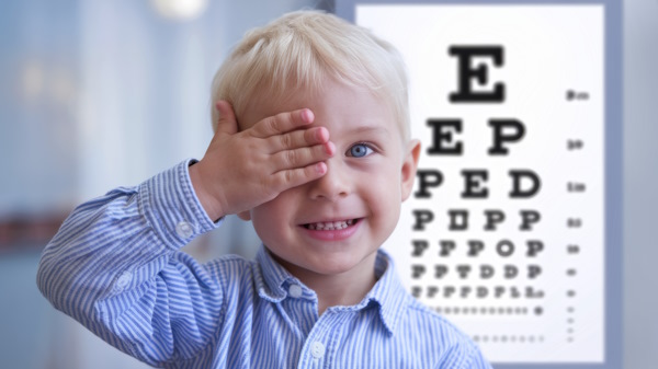 Jeune garçon souriant avec une main cachant un oeil et charte de test visuel en arrière plan